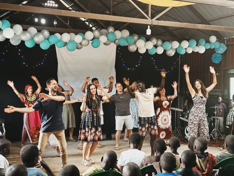 Many adults are on a stage and dance, swinging their arms in the air. Some children are watching them.